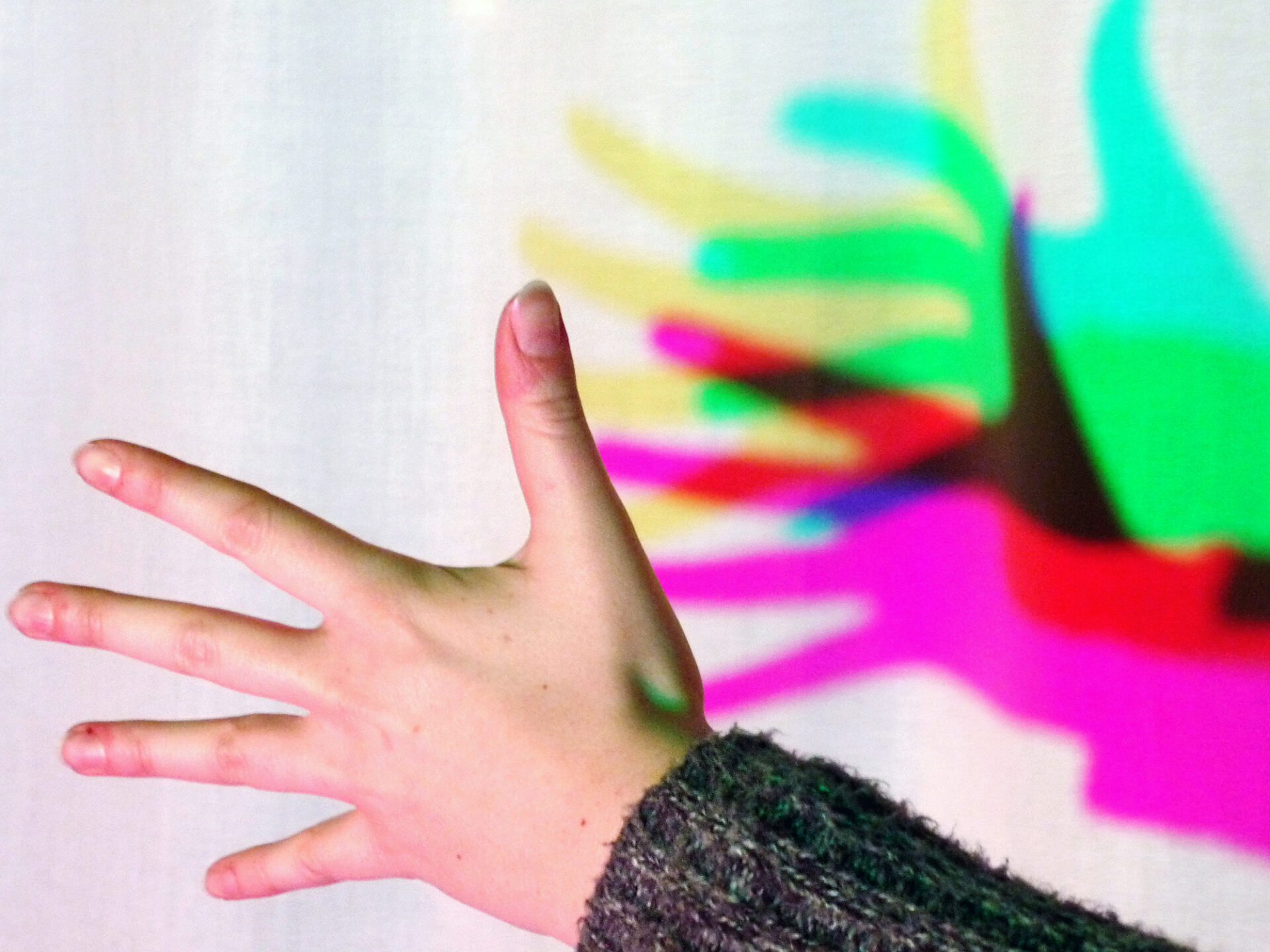Eine Hand wirft farbige Schatten auf einen weißen Hintergrund