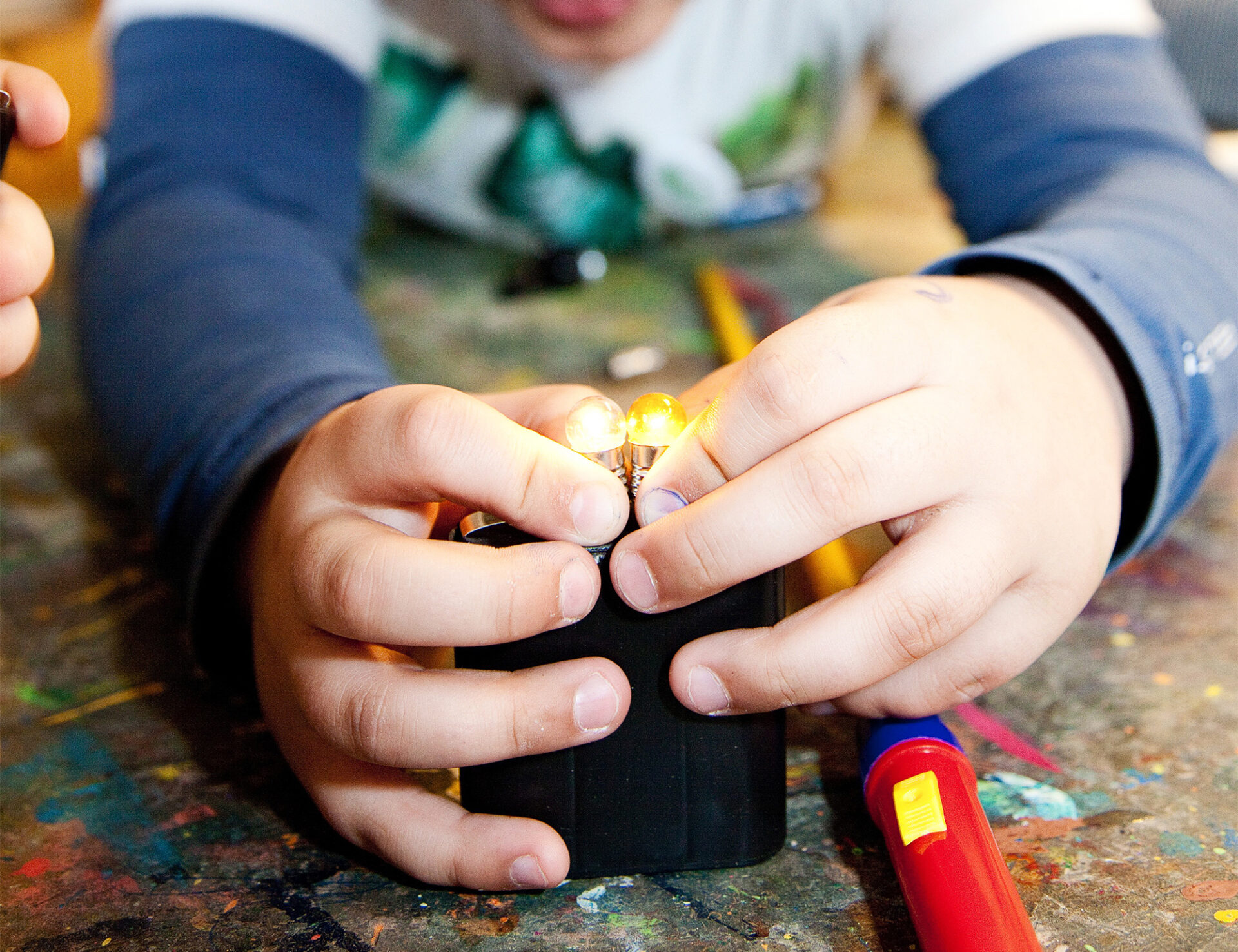 Ein Kind bringt zwei Glühbirnchen mit Hilfe einer 4,5-Volt-Batterie zum Leuchten