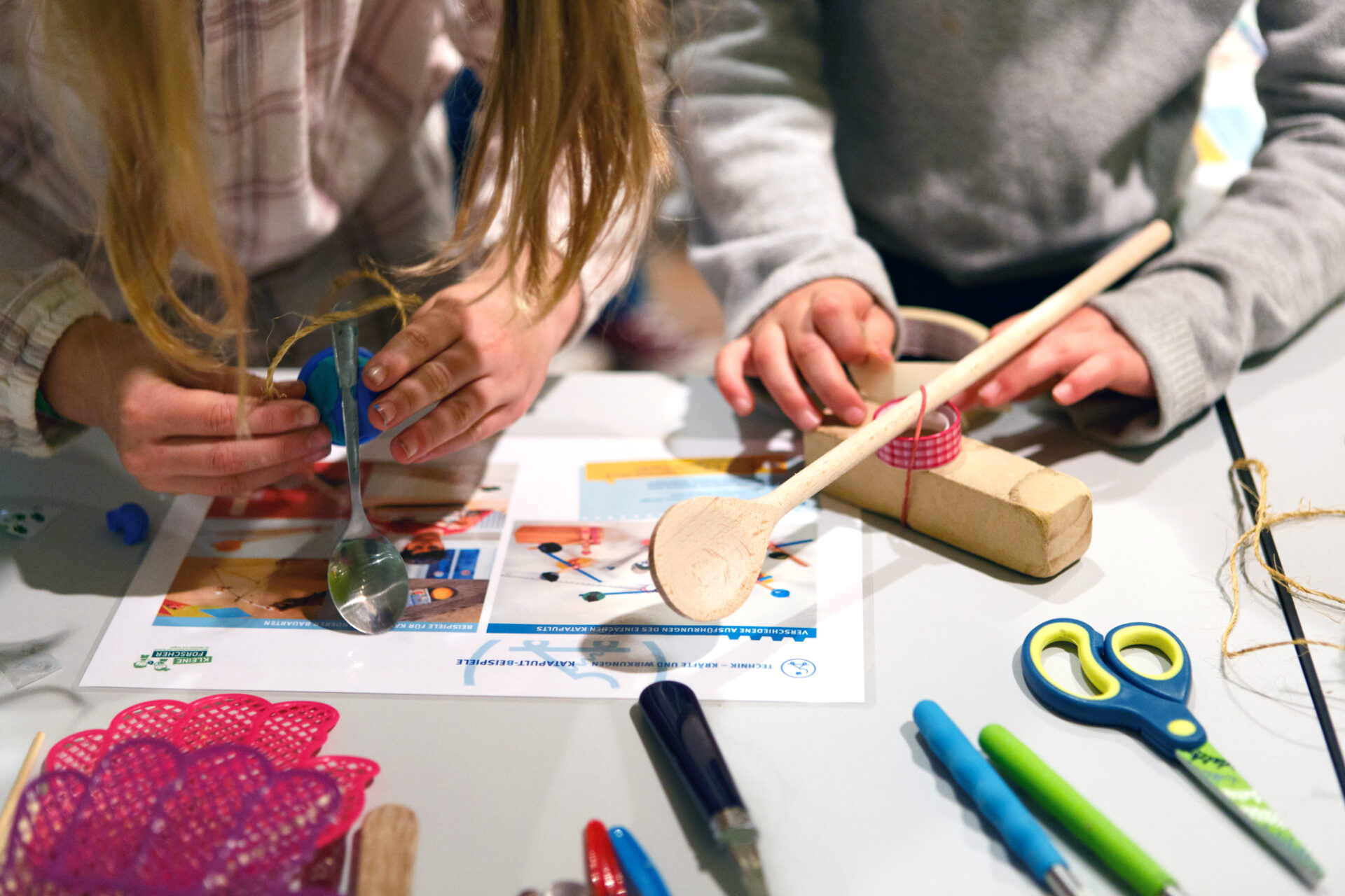 Kinder bauen Katapulte aus Alltagsmaterialien wie Löffeln, Klebeband und Flaschendeckeln