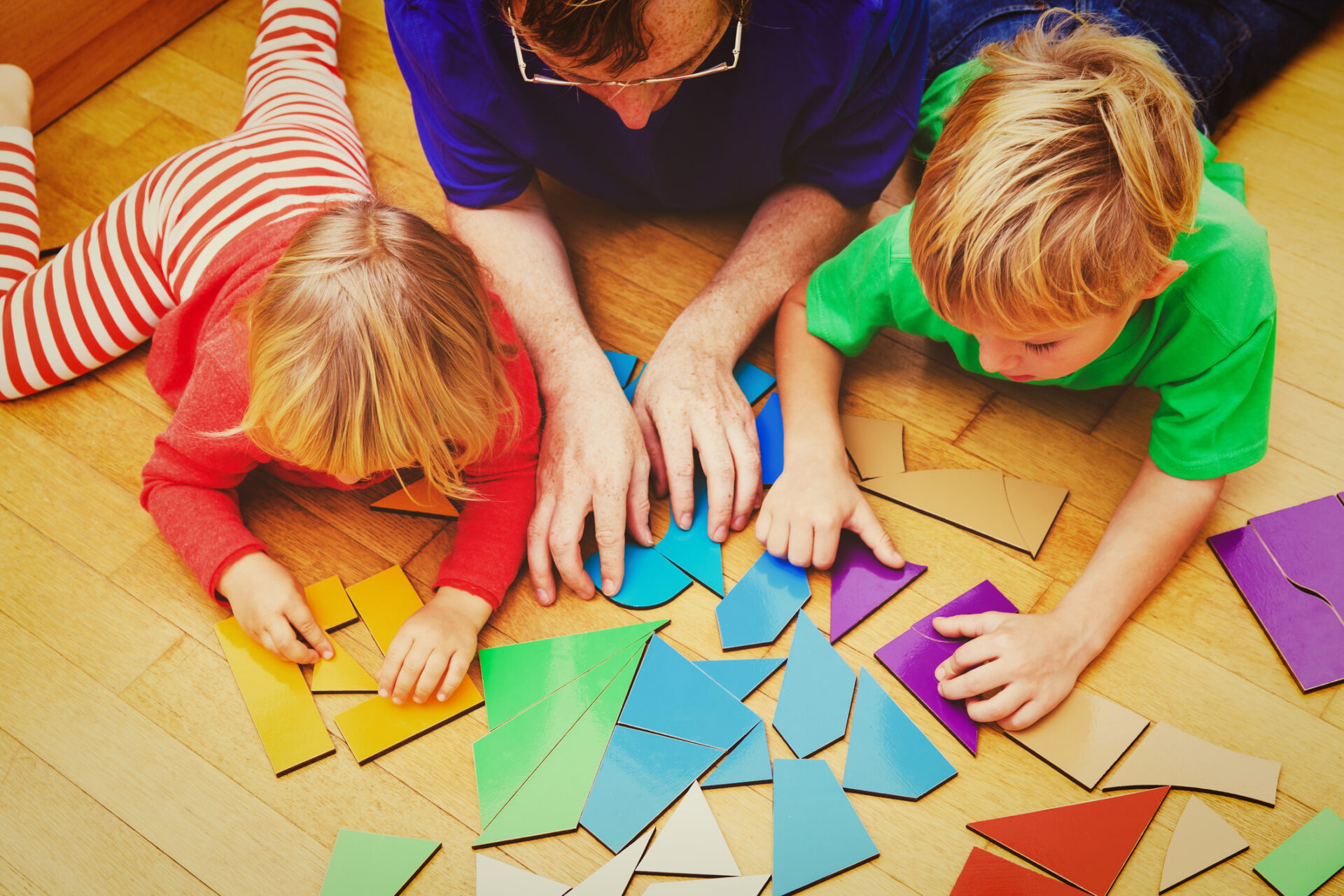 Zwei Kinder und eine erwachsene Person spielen mit geometrischen Formen